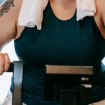 Recall Training - Smiling plus size female with towel exercising on cross trainer machine while looking at camera during workout in fitness studio