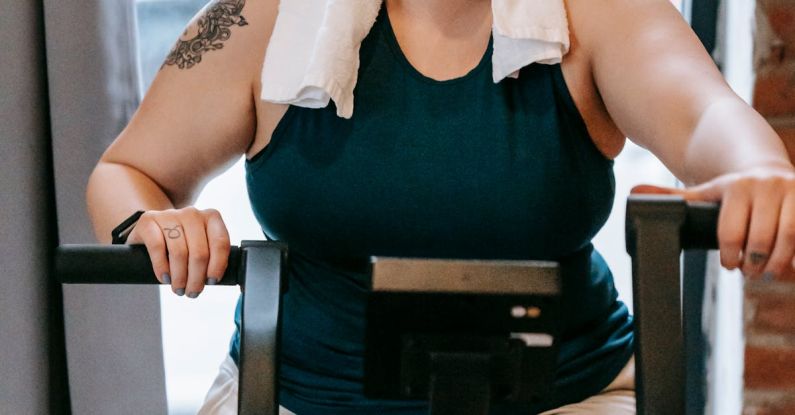 Recall Training - Smiling plus size female with towel exercising on cross trainer machine while looking at camera during workout in fitness studio